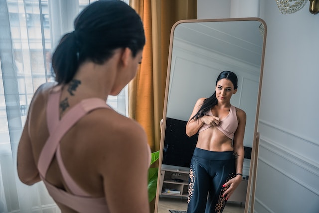 Žena si prohlíží své tělo v zrcadle.
